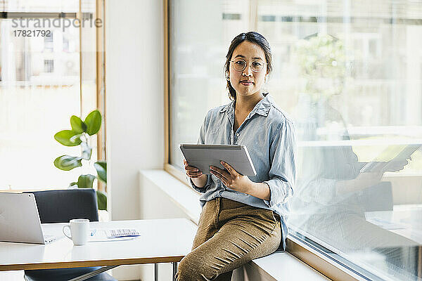Lächelnde Geschäftsfrau mit Tablet-PC sitzt auf der Fensterbank