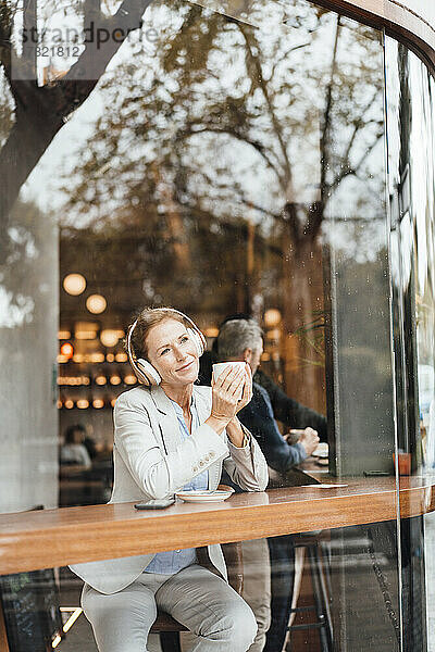 Geschäftsfrau hält Kaffeetasse in der Hand und genießt Musik  die über drahtlose Kopfhörer im Café hört