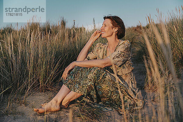Glückliche Frau sitzt neben Pflanzen am Strand