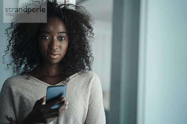 Junge Frau mit lockigem Haar hält Mobiltelefon in der Hand