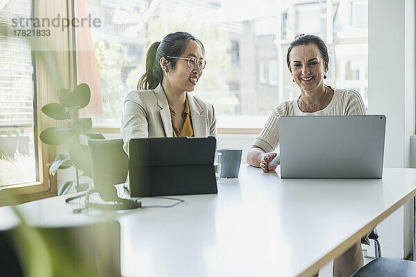 Glückliche reife Geschäftsfrau mit Kollegin  die im Büro am Laptop diskutiert