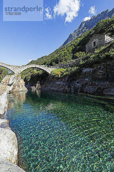 Schweiz  Tessin  Lavertezzo  klare Oberfläche des Flusses Verzasca mit der Bogenbrücke Ponte dei Salti im Hintergrund