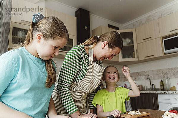 Happy girl with mother and sister preparing food in kitchen at home