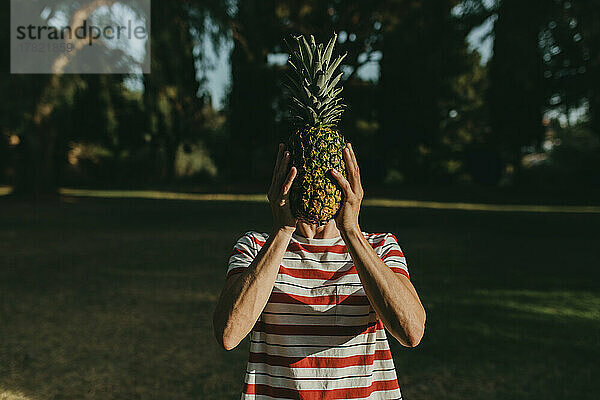 Frau bedeckt Gesicht mit Ananas im Park