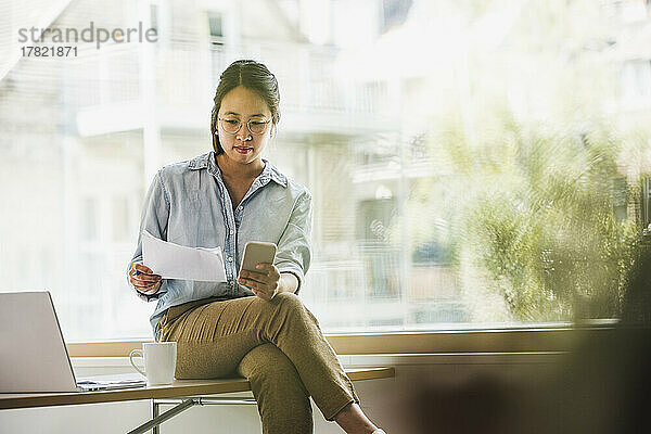 Geschäftsfrau mit Dokument und Smartphone im Büro