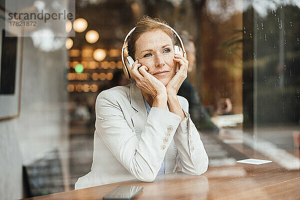 Geschäftsfrau mit Kopf in den Händen  die im Café Musik hört und durch Glas gesehen wird