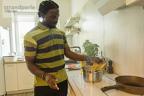Junger Mann legt ungekochte Spaghetti in den Kochtopf in der Küche