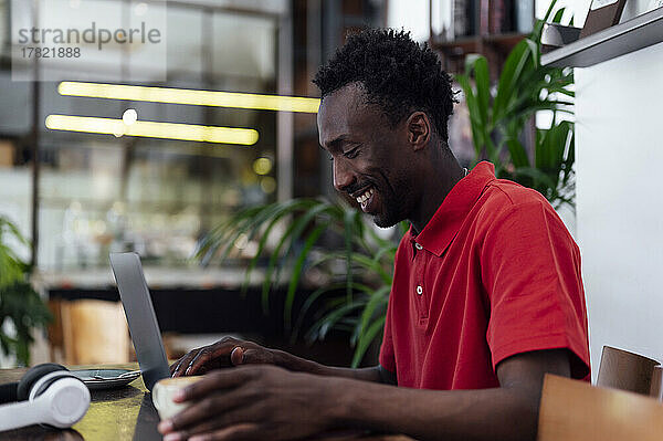 Lächelnder Mann mit Kaffeetasse und Laptop im Café