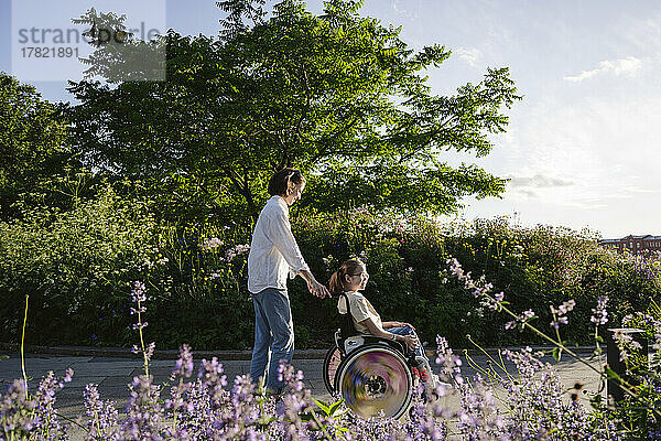 Mutter schiebt Tochter mit Behinderung  die im Rollstuhl im Park sitzt