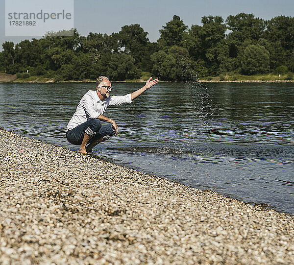 Lächelnder Mann  der am Flussufer mit Wasser spielt