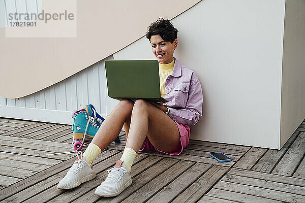 Glückliche Frau sitzt mit Laptop vor der Wand