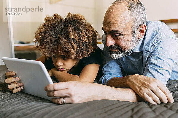 Father sharing tablet PC with boy lying on bed at home