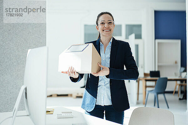 Glückliche Geschäftsfrau mit Solarpanel auf Musterhaus im Büro