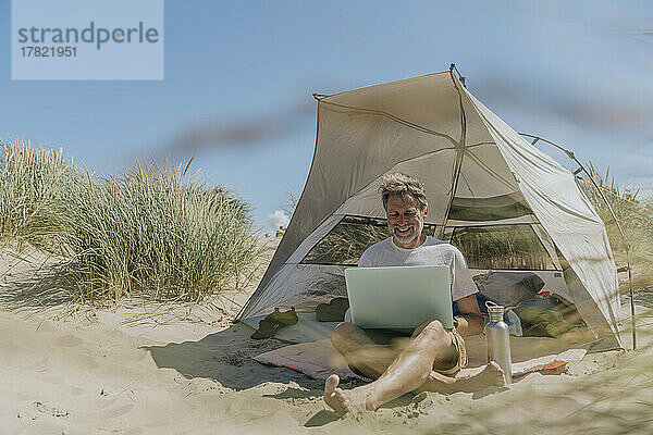 Glücklicher Freiberufler  der an einem sonnigen Tag im Zelt sitzt und seinen Laptop benutzt