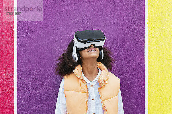 Mädchen mit Virtual-Reality-Simulator steht vor einer bunten Wand