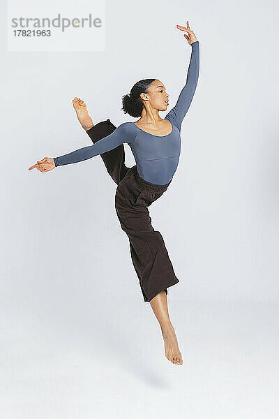 Junge klassische Balletttänzerin springt mit erhobenen Armen vor weißem Hintergrund