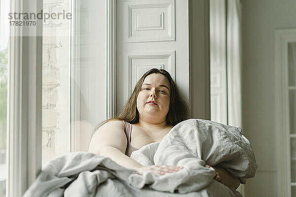 Frau mit Decke sitzt zu Hause am Fenster