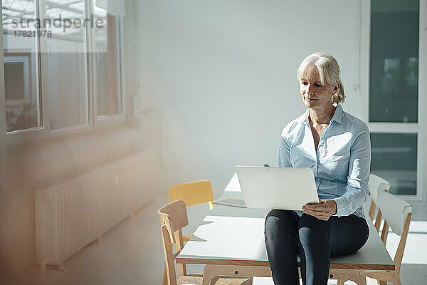 Senior businesswoman using laptop sitting on desk in office