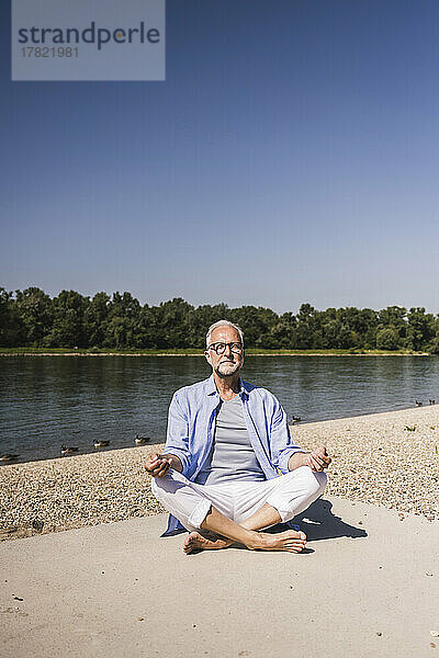 Lächelnder älterer Mann meditiert am Flussufer