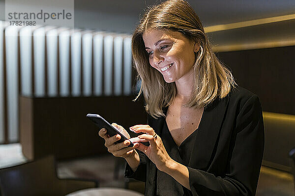 Glückliche Geschäftsfrau nutzt Smartphone in der Lobby des Hotels