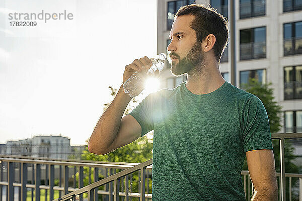 Junger Mann trinkt Wasser an einem sonnigen Tag