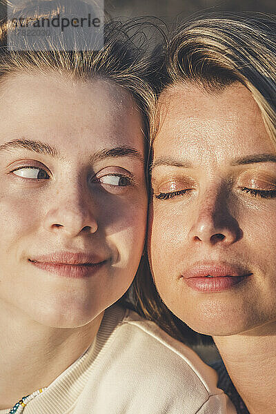 Smiling teenage girl looking at mother with eyes closed