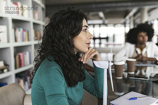 Geschäftsfrau mit Windturbinenmodell sitzt am Schreibtisch