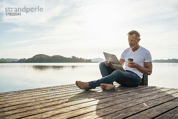 Reifer Mann liest Zeitung und trinkt Kaffee am Pier am See