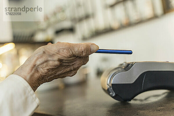 Hand einer älteren Frau  die im Café per Smartphone bezahlt