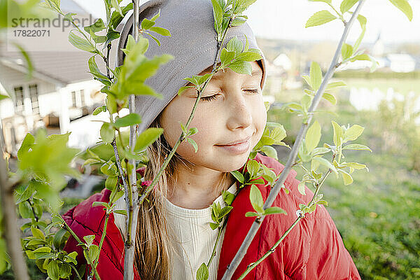 Lächelndes Mädchen mit geschlossenen Augen durch Pflanze im Garten