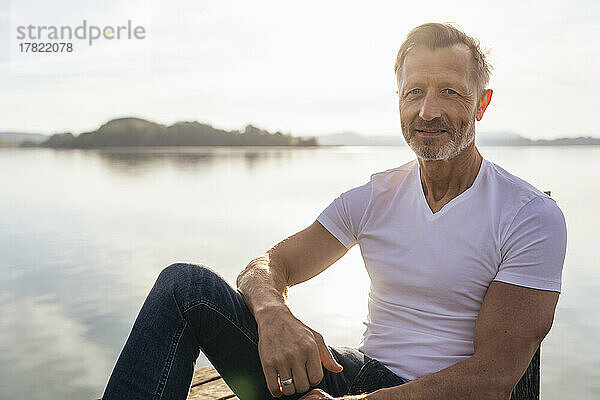 Lächelnder reifer Mann  der an einem sonnigen Tag am See sitzt