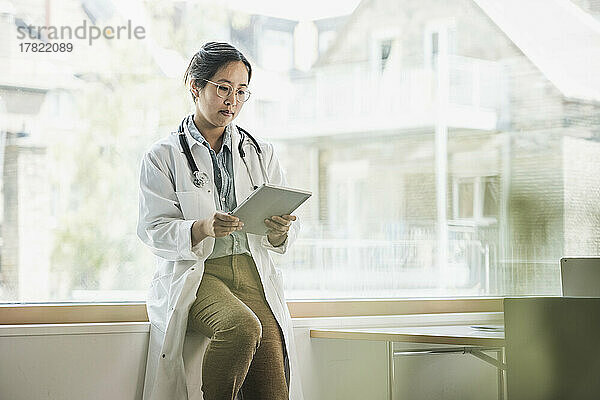 Arzt sitzt mit Tablet-PC auf der Fensterbank