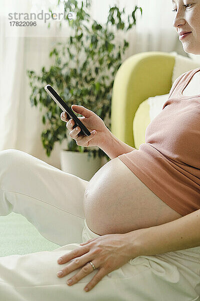 Lächelnde schwangere Frau  die zu Hause ihr Smartphone benutzt