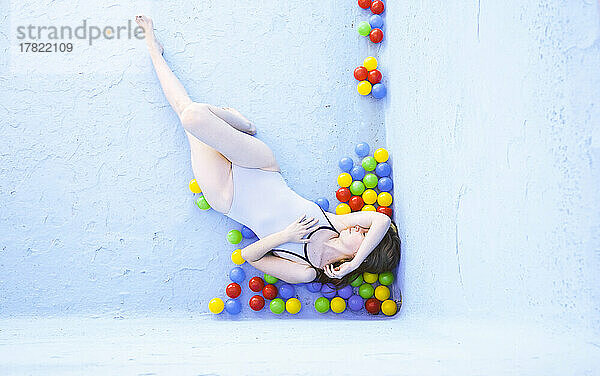 Woman lying with multi colored plastic balls in empty swimming pool