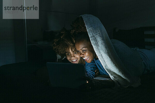 Glückliche Mutter und Tochter teilen sich zu Hause unter der Decke einen Tablet-PC