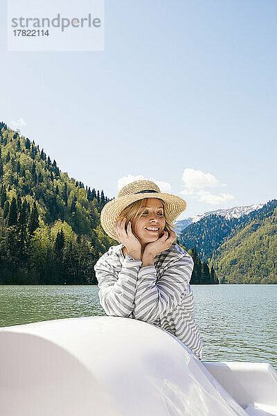 Lächelnde Frau mit Hut genießt an einem sonnigen Tag eine Bootsfahrt im Ritsa-See