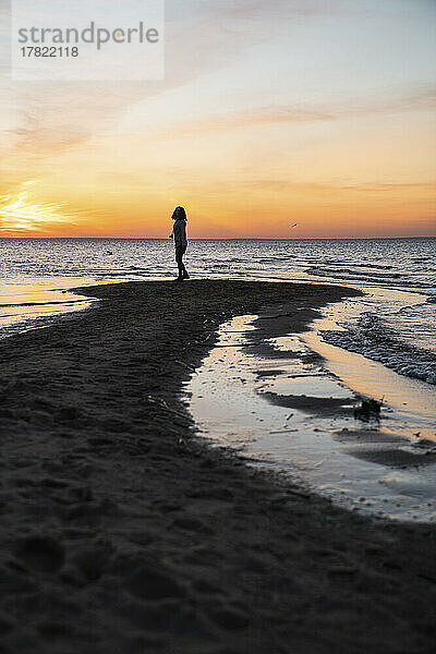 Young woman standing on sea coast at sunset