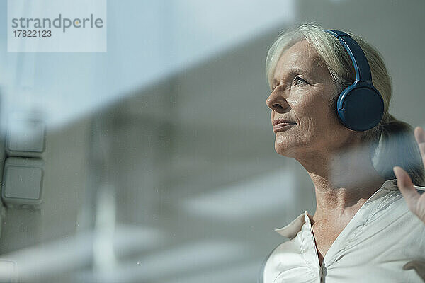 Smiling senior woman listening music through wireless headphones