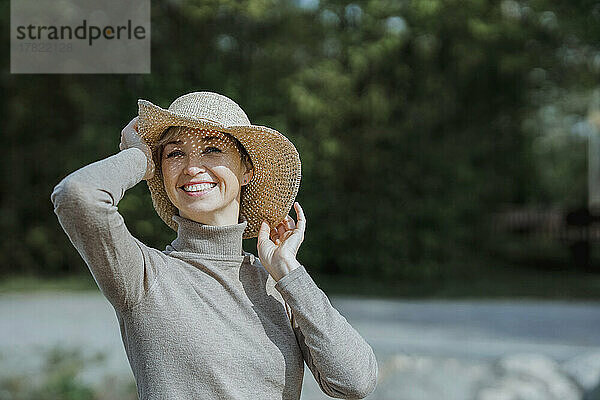 Glückliche reife Frau mit Hut an einem sonnigen Tag
