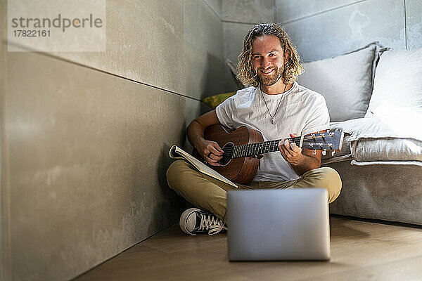 Lächelnder Komponist  der zu Hause Gitarre spielt