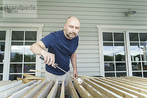 Mann bemalt Bretter mit Walze im Hinterhof