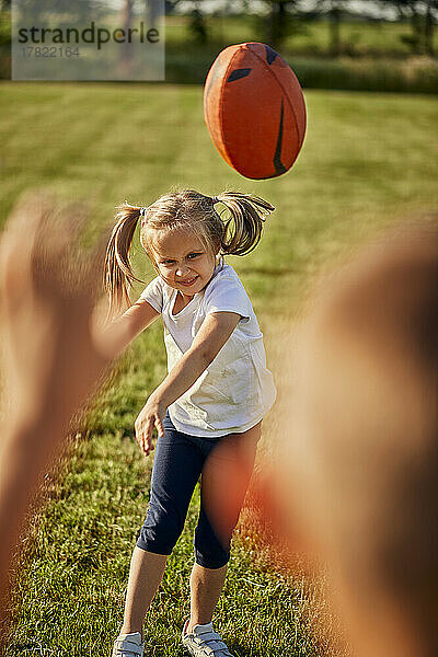 Lächelndes Mädchen wirft seinem Bruder an einem sonnigen Tag Rugbyball zu