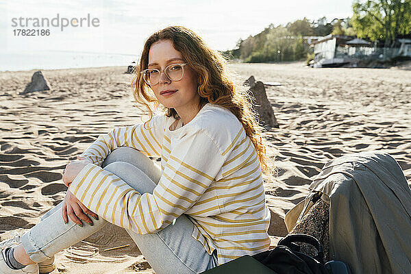 Frau sitzt an sonnigem Tag am Strand