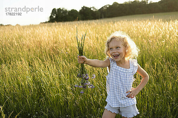 Glückliches Mädchen  das mit der Hand auf der Hüfte steht und einen Blumenstrauß auf dem Feld hält