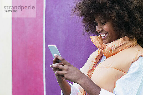 Fröhliches Mädchen mit Smartphone  das an einer bunten Wand steht
