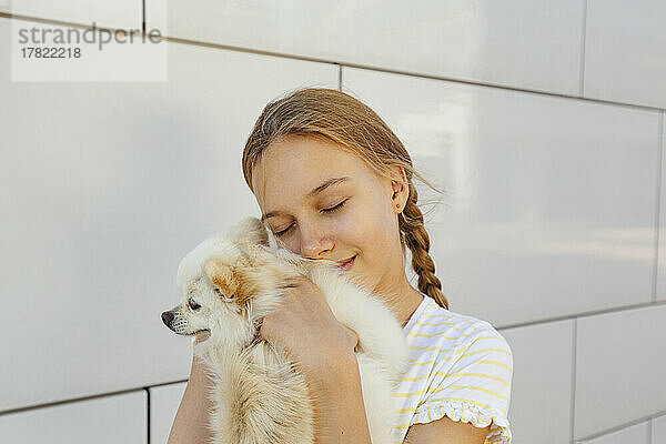 Lächelndes Mädchen umarmt Hund vor der Wand