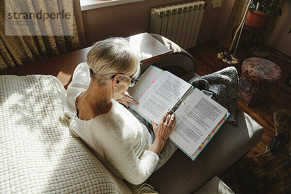 Ältere Frau liest Dokument und sitzt zu Hause auf dem Sofa