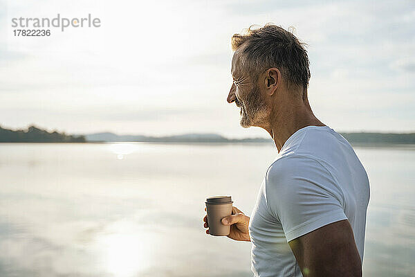 Reifer Mann hält an einem sonnigen Tag eine Einwegkaffeetasse am See