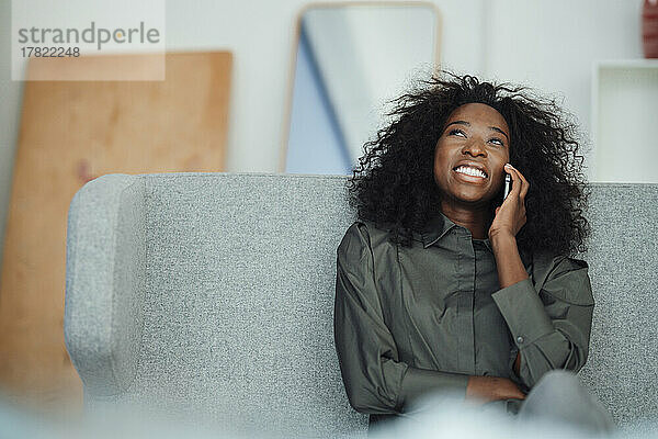 Happy young woman talking through mobile phone sitting on sofa