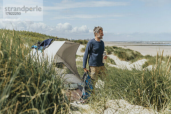 Happy mature man camping on sunny day at beach